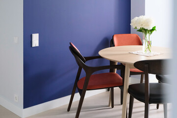 wooden table with peony flowers and chairs near colorful wall in modern empty dining room