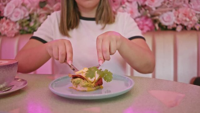 A woman prepares to eat eggs benedict in a stylish cafe with pink floral decor.