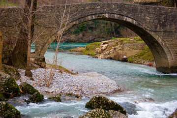 Blue clear river with a rocky bank under an ancient stone bridge