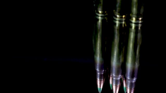 Rifle bullets rotate and cast their reflection on the glass table with a black background and cinematic look