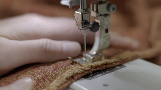 This video shows a close up view of red upholstery fabric being sewn on a sewing machine. 