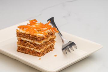 Carrot cake with layers of cream cheese and topped with fresh shredded carrot