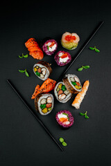 Various sushi, Japanese  lunch and side dishes and dipping teriyaki sauce on dark background. Side view of portion of Japanese sushi rolls set. Asian cuisine. Free space for your text.