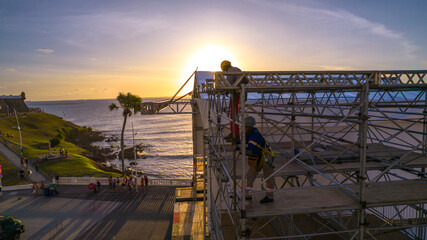 Naklejka premium Workers assembling metal structure with the ocean and sunset in the background