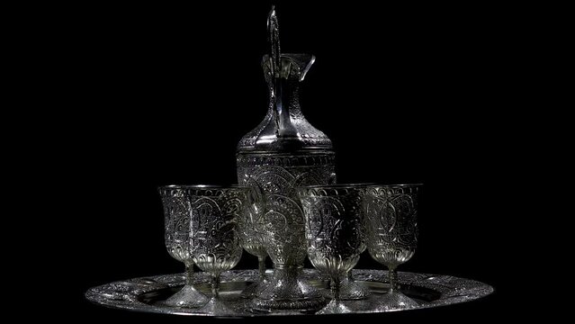 A silverware set, with handmade cultural and traditional South Asian designs, rotating on an automatic display stand in a black background and cinematic indoor light. 