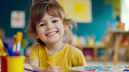 little preschool girl smiling, sits at the table and painting in kindergarten