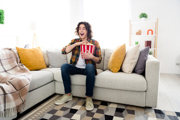 Full length photo of impressed excited guy wear plaid shirt watching interesting movie eating pop corn indoors room home house