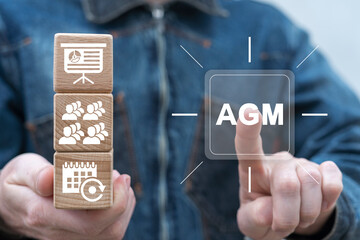 Man holding wooden cubes with icons presses virtual button with abbreviation: AGM. Annual General Meeting of shareholders. AGM Annual General Meeting Business Corporate Management Concept.