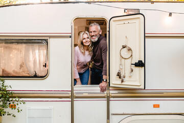 Cheerful happy elderly couple spouses husband and wife standing on the porch of their motor home...
