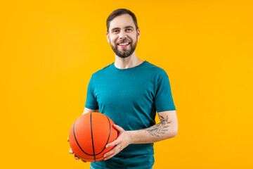 Studio portrait of young attractive smiling basketball fan or player posing over bright colored orange yellow background with a ball in hands - 725861105