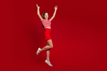 Fototapeta na wymiar Full length photo of funny excited lady dressed striped top mini skirt jumping high rising hands arms empty space isolated red color background