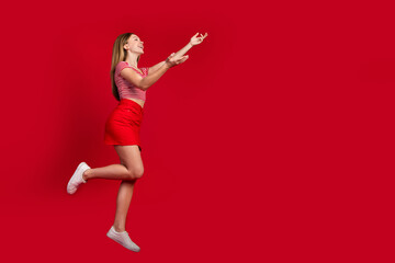 Fototapeta na wymiar Full length photo of pretty funny lady dressed striped top mini skirt jumping high catching arms empty space isolated red color background