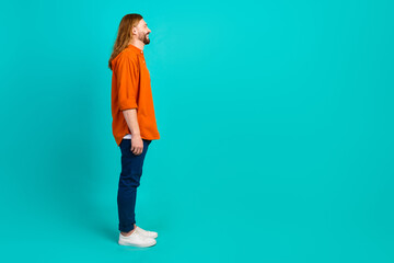 Side photo of optimistic blond hair guy in orange shirt looking at billboard advertisement place isolated on cyan color background