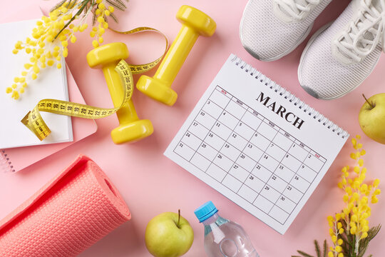Spring into action: Your personalized fitness schedule. Top view photo of calendar, notepads, apple, sneakers, water bottle, sport equipment, mimosa on pastel pink background