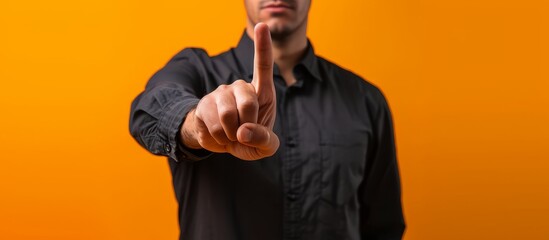 Closeup of a dark-haired man in a black shirt displaying the number one with his finger, isolated on an orange background.