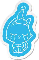 Fototapeta premium crying cartoon sticker of a cat sitting wearing santa hat