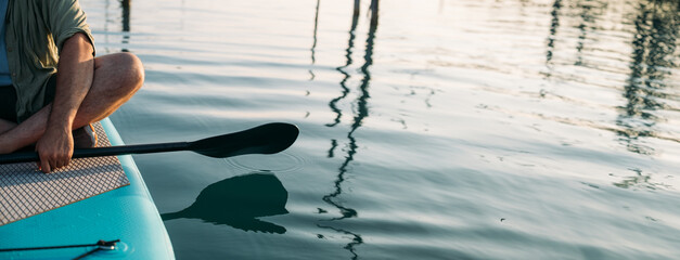 Close-up of paddles over calm water and surfboards at sunset.
