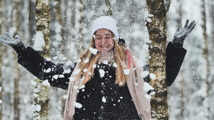 A girl is walking through the woods and kicking up snow in a birch forest.
