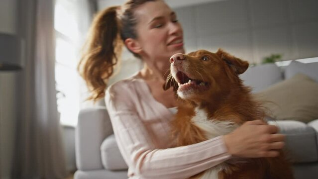 Woman hugging adorable dog with happy smile at home close up. Girl caressing pet
