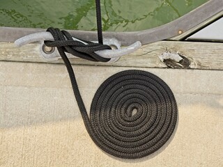Coiled black braided rope hitched to cleat on dock deck above green tropical water