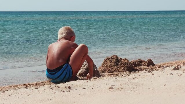 A boy plays a sand constructor, spending healthy leisure time on the Black Sea beach. A child builds a sand castle. A boy who builds a sand fortress on the seashore on a sunny day. 4K