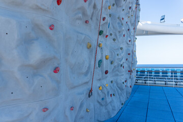 Fototapeta na wymiar Rock climbing wall on a cruise ship. Colorful climbing holds a safety rope. Ocean horizon. 