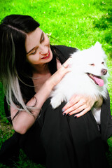 Brunette young girl in black clothes walking in the green par with a white pomeranian funny dog