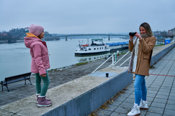 With a compact camera in hand, the mother captures the exuberance of her daughter on the quayside,...