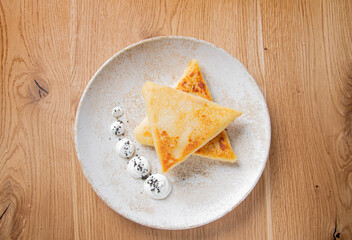 pancakes with creamy sauce on a light plate on a wooden table