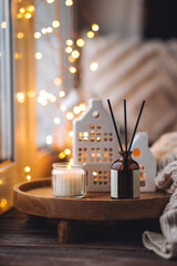 Aroma diffuser, burning candle, Christmas perfume on wooden bamboo tray, knitted sweater. Cozy home decor, hygge and aromatherapy concept. Comfortable atmosphere, Scandinavian decor.