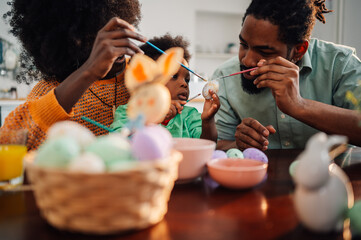 Mother, father and their little son painting and decorating eggs for holiday