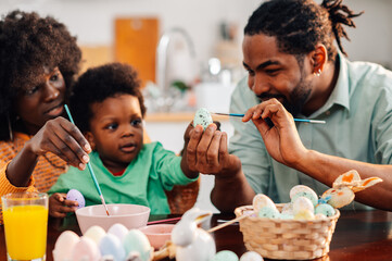 Happy african american family painting easter eggs together at home