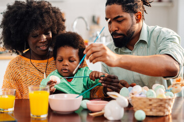 An interracial family sitting at home on easter saturday and painting eggs.