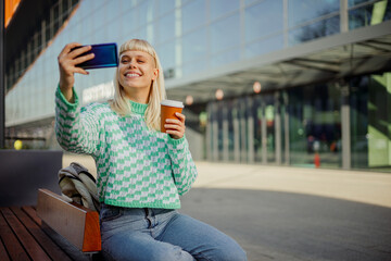Fototapeta premium A young urban girl is sitting on a city street and taking selfies.