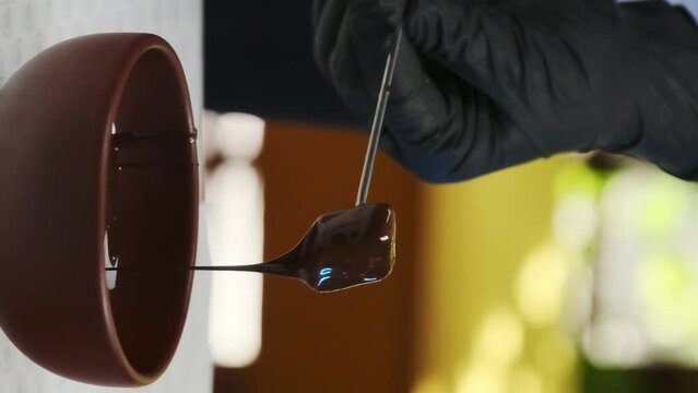 Process of dipping candy on metal fork into plate with melted chocolate closeup. Workshop from professional culinarian in confectionery
