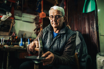 Portrait of a senior cobbler at his shop working with shoes.
