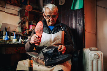 A senior artisan is sitting at his cobbler workshop and repairing boots.