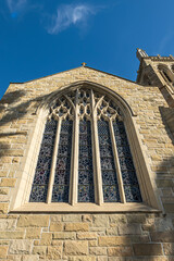 Naklejka premium Santa Barbara, CA, USA - November 30, 2023: Trinity Episcopal Church, closeup of large stained glass window set in sculpted stone frame on State Street. Part of tower. Blue cloudscape
