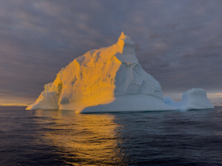A huge high breakaway glacier drifts in the southern ocean off the coast of Antarctica at sunset, the Antarctic Peninsula, the Southern Arctic Circle, azure water, cloudy weather