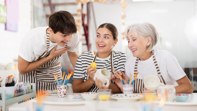 Group of cheerful people painting ceramic dishware in pottery class. High quality photo
