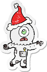 distressed sticker cartoon of a cyclops alien spaceman pointing wearing santa hat