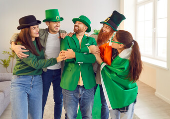 Happy excited young friends in green hats and clothes standing in a row in the living room at home...