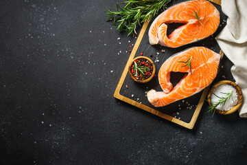 Fresh fish. Salmon steaks on cutting board at black background. Top view with ingredients for...