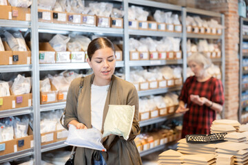 Young woman in casual clothes chooses package of dry clay for making pottery in pottery shop