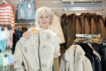 Mature lady carefully inspects fur coats, contemplating which one best complements her winter wardrobe.
