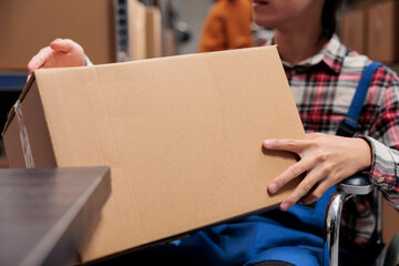 Postal service worker with disability holding package while working in warehouse. Shipment company...