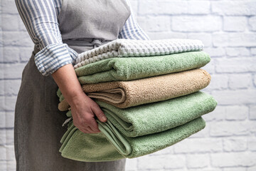 maid holds a stack of bath towels against a white brick wall. Close-up.