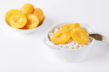 Fresh cottage cheese in white bowl with apricot pieces on white background