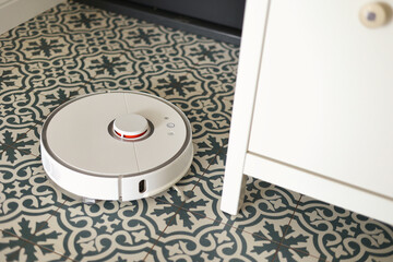 Wireless autonomous smart robotic vacuum cleaner is vacuuming floor with modern tiles at living room. Self-propelled cleaning robot. Floor cleaning system. Household remote control appliances.
