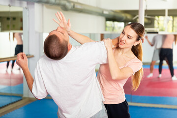 Young woman paired up with male partner in self defense training, practicing basic palm strike..